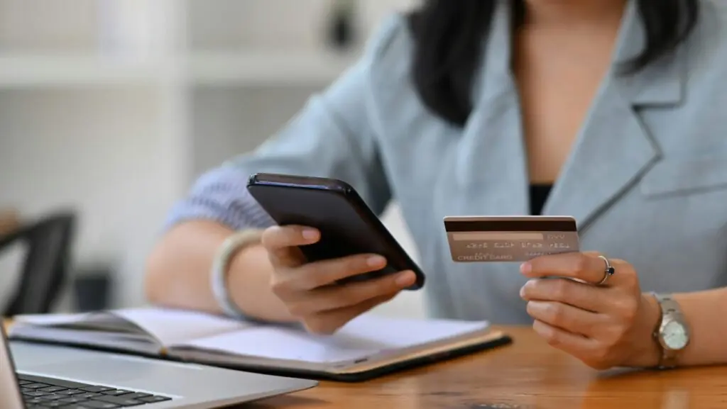 woman holding phone and credit card in front of laptop